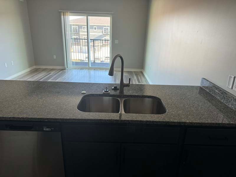 Kitchen with stainless steel sink, granite countertop, dark cabinets, and sliding glass door to a balcony.