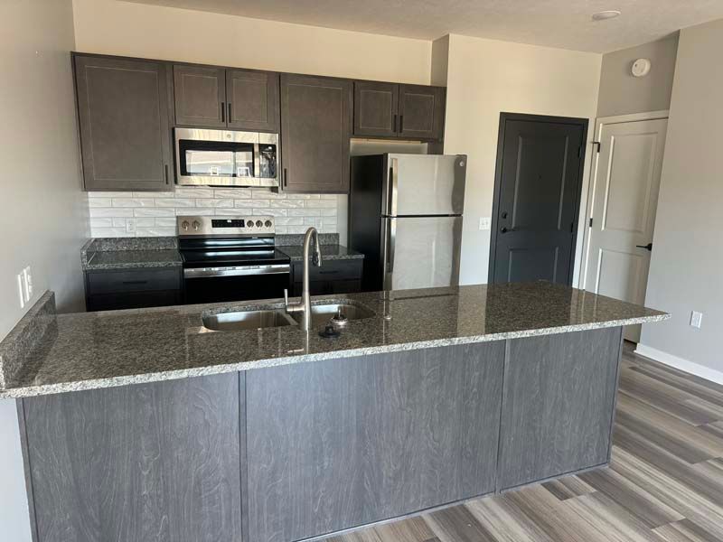 Modern kitchen with gray cabinets, stainless steel appliances, granite countertops, and an island.