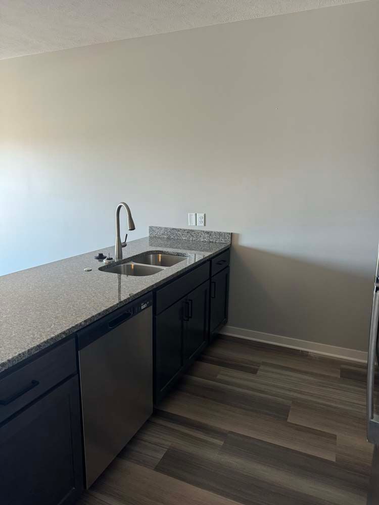 Kitchen island with stainless steel sink, dishwasher, dark cabinets, and granite countertop. Dark wood flooring.