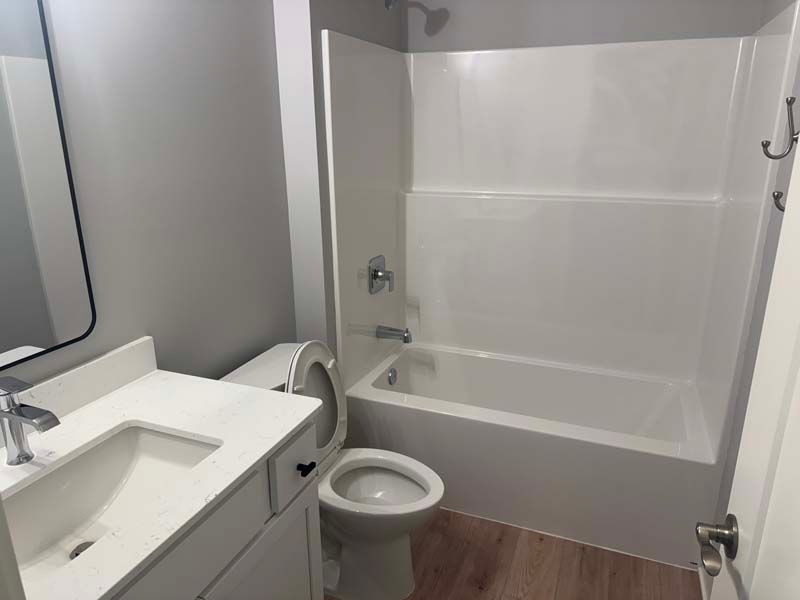 Bathroom with white bathtub, toilet, sink, and gray walls; wooden floor.