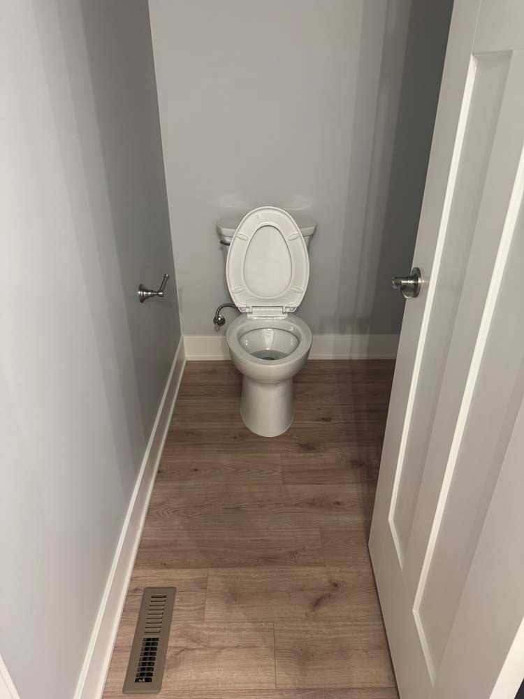 Small bathroom with toilet, open door, wood-look floor, and gray walls.