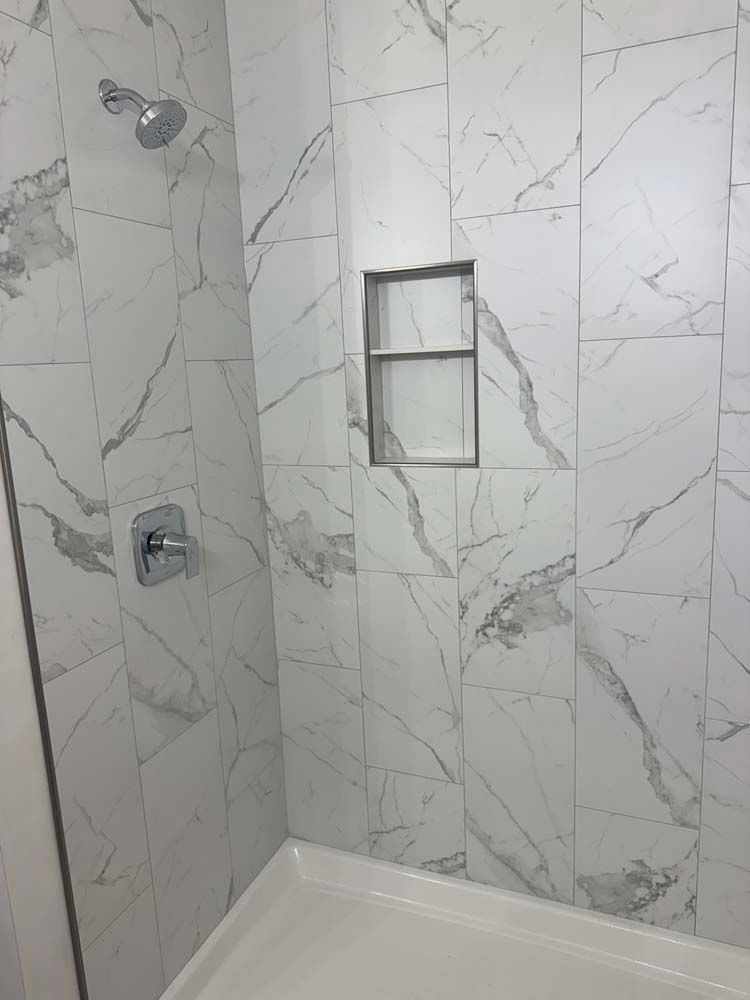 White marble-tiled shower with a built-in shelf and silver shower fixtures.