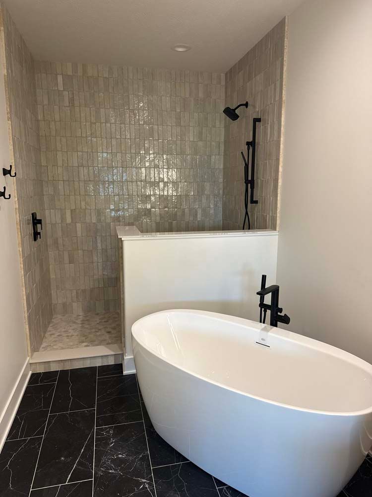 Bathroom with white soaking tub, walk-in shower with grey tile, and black fixtures.