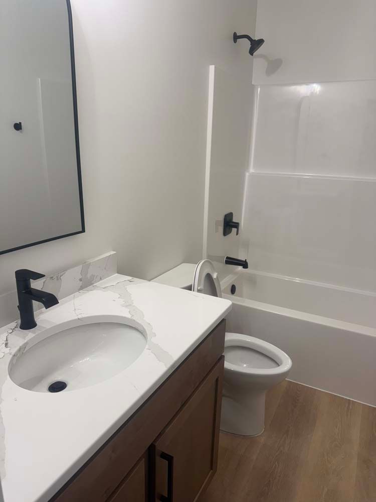 Bathroom with white tub, toilet, and vanity with black fixtures and a large mirror.