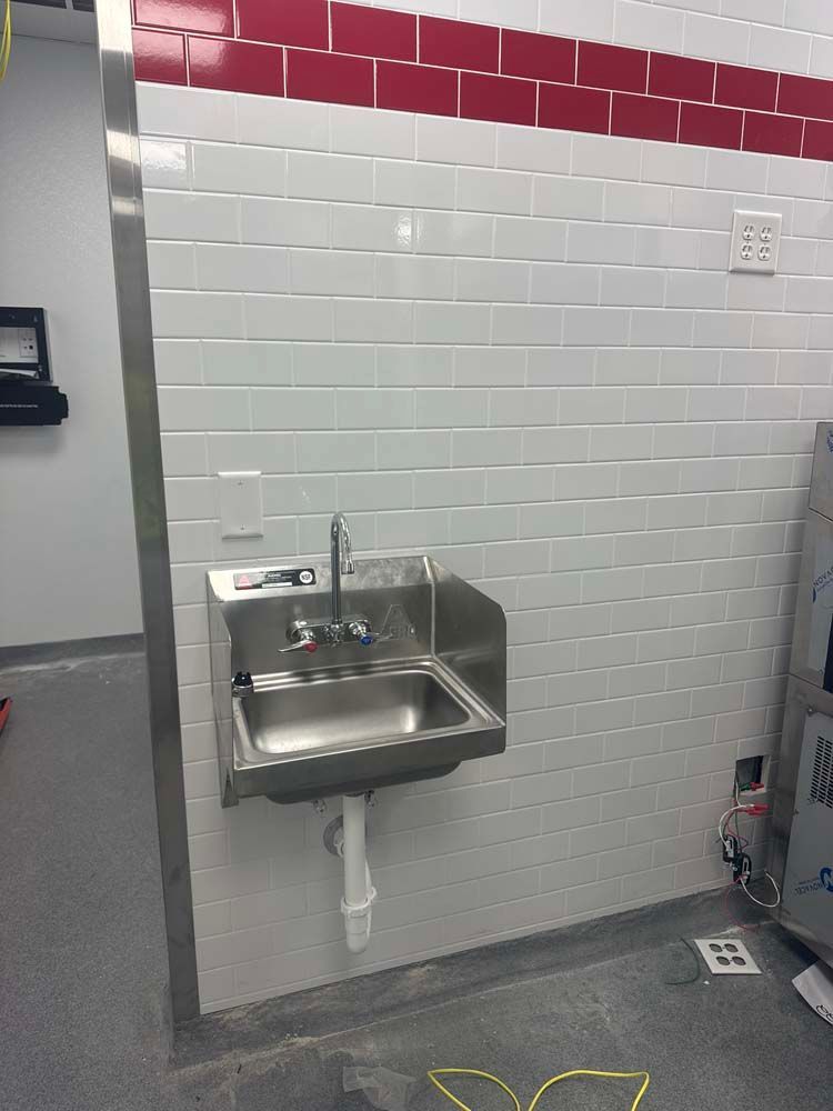 Stainless steel sink in a corner, on white brick wall with red trim. Electrical outlet above.