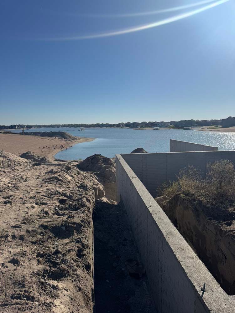 Concrete wall construction near a body of water under a clear, sunny sky.