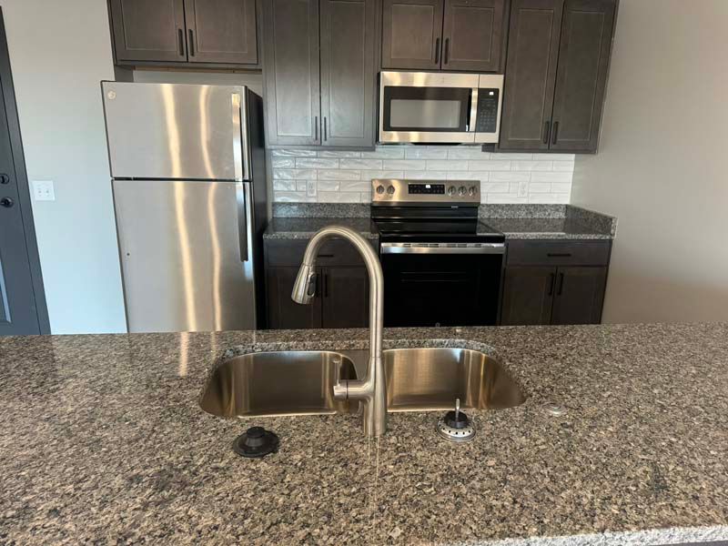 Kitchen with stainless steel appliances, dark cabinets, granite countertop, and a double sink.
