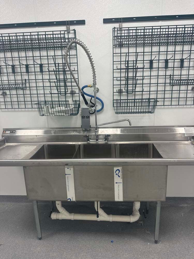 Stainless steel triple sink with overhead sprayer, in a commercial kitchen.