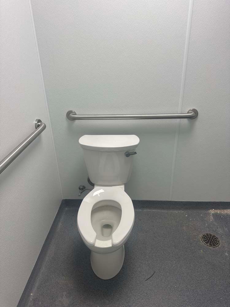 Toilet in a public restroom with grab bars, gray walls, and flooring.