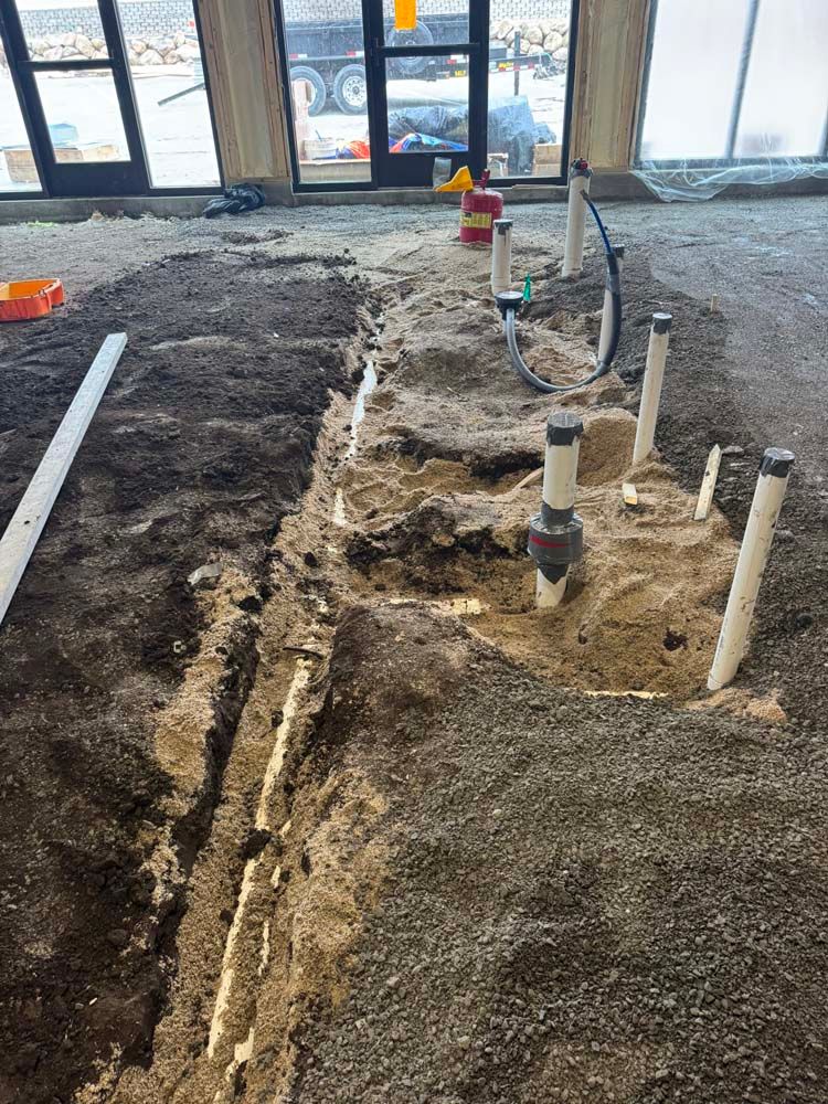 Construction site with excavated trench showing plumbing pipes and fittings.