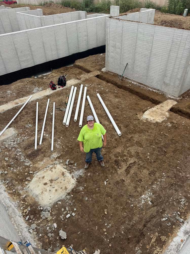 Person stands in construction site with concrete foundation walls, white pipes.