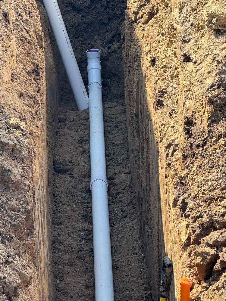 White PVC pipes installed vertically in a narrow, freshly dug trench.