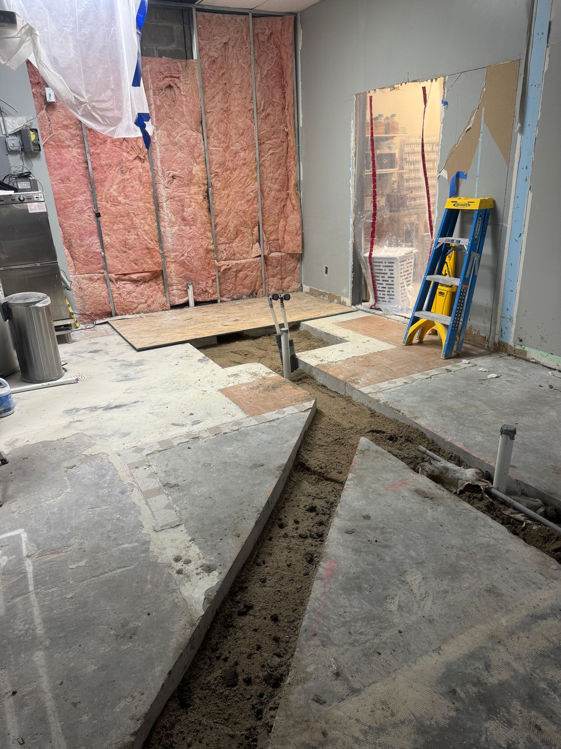 Construction site: concrete floor with trenches, exposed insulation, open doorway, and a ladder.