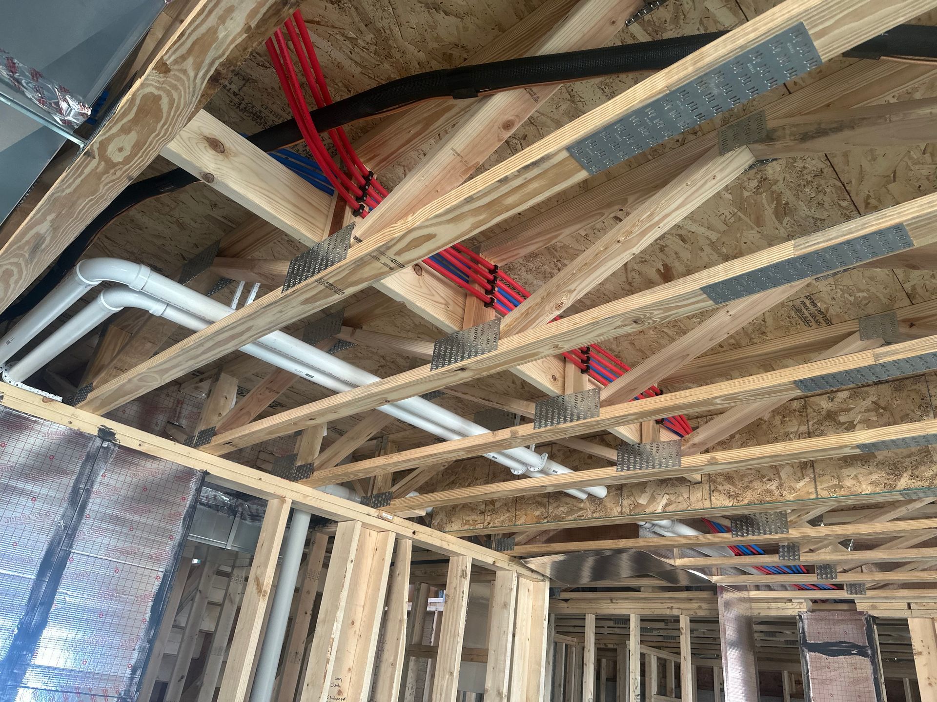 Wooden ceiling under construction with red and white pipes and black wiring.