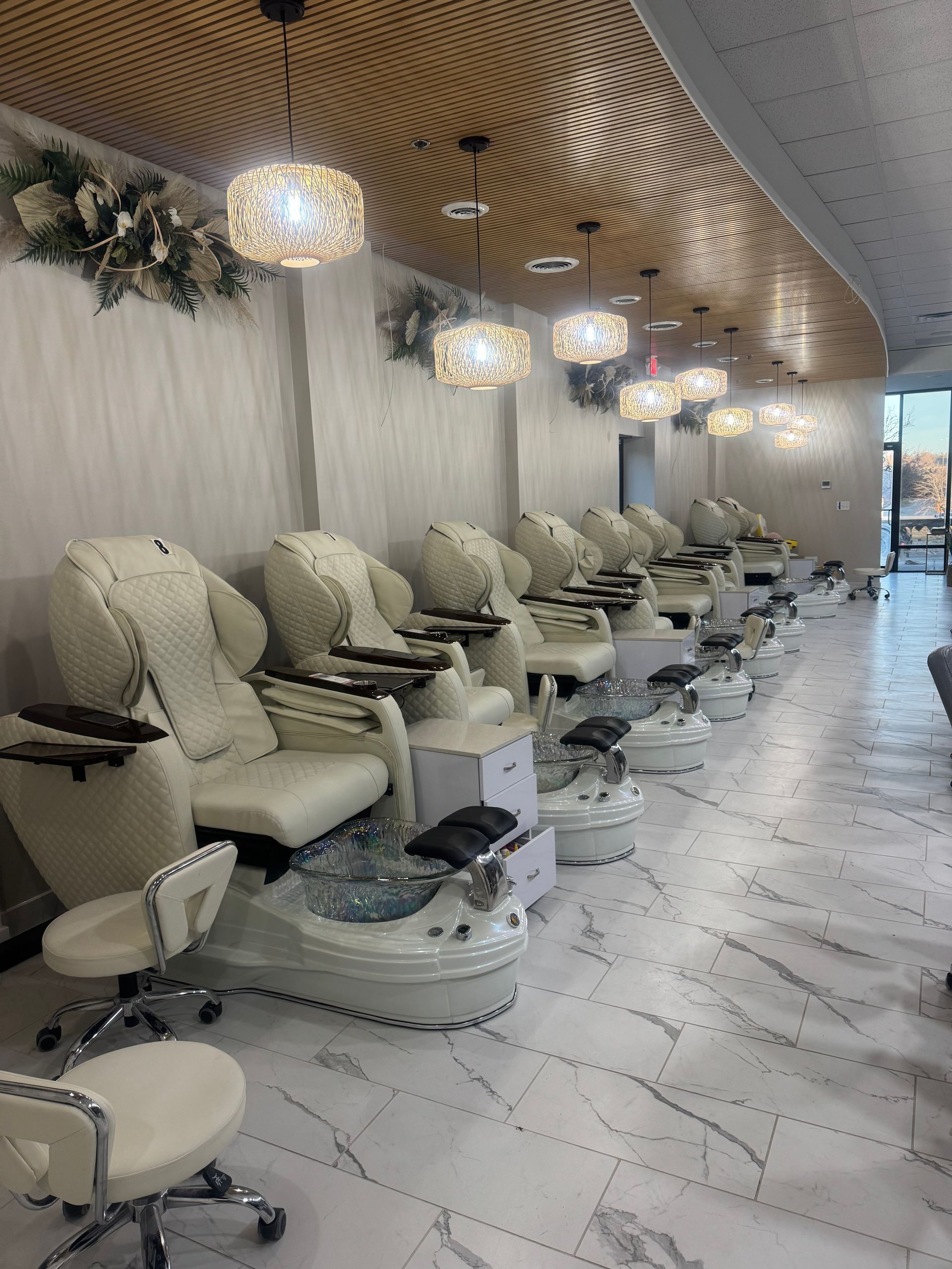Interior of a nail salon with white pedicure chairs, marble flooring, and decorative lighting.