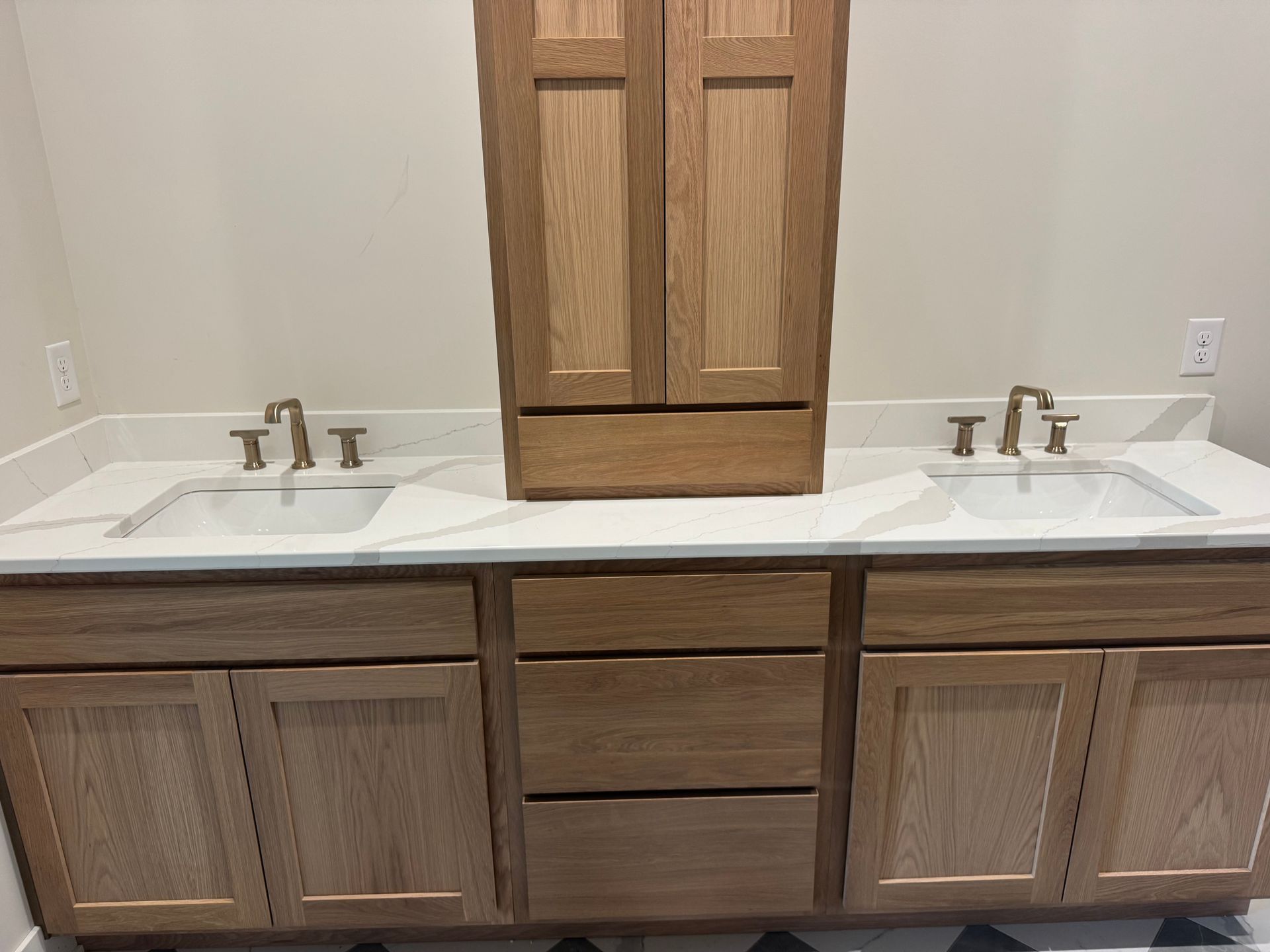 Bathroom with light wood double vanity, white countertops, sinks, and tall cabinet.