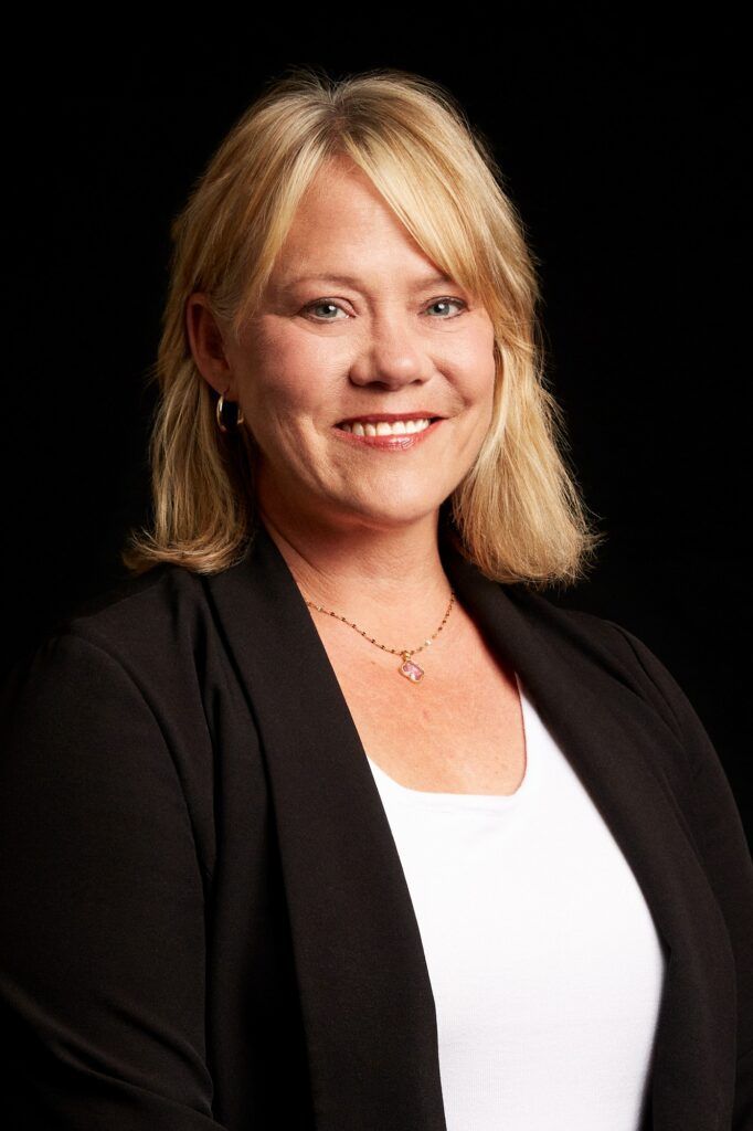 A woman wearing a black jacket and a white shirt is smiling for the camera.