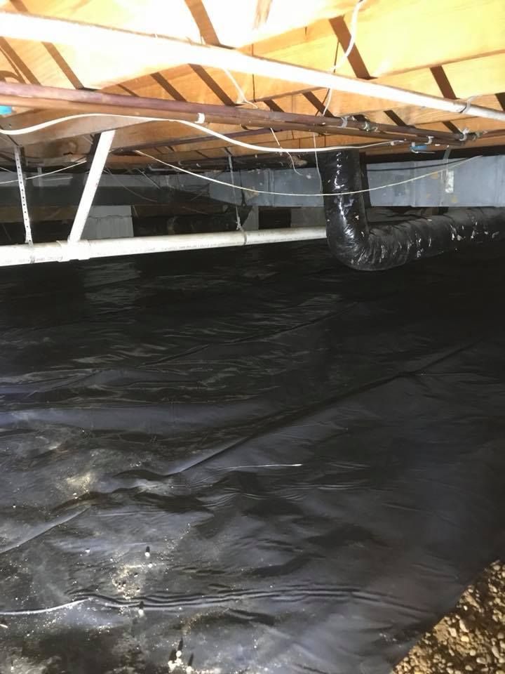 A crawl space under a house with a black tarp on the floor.