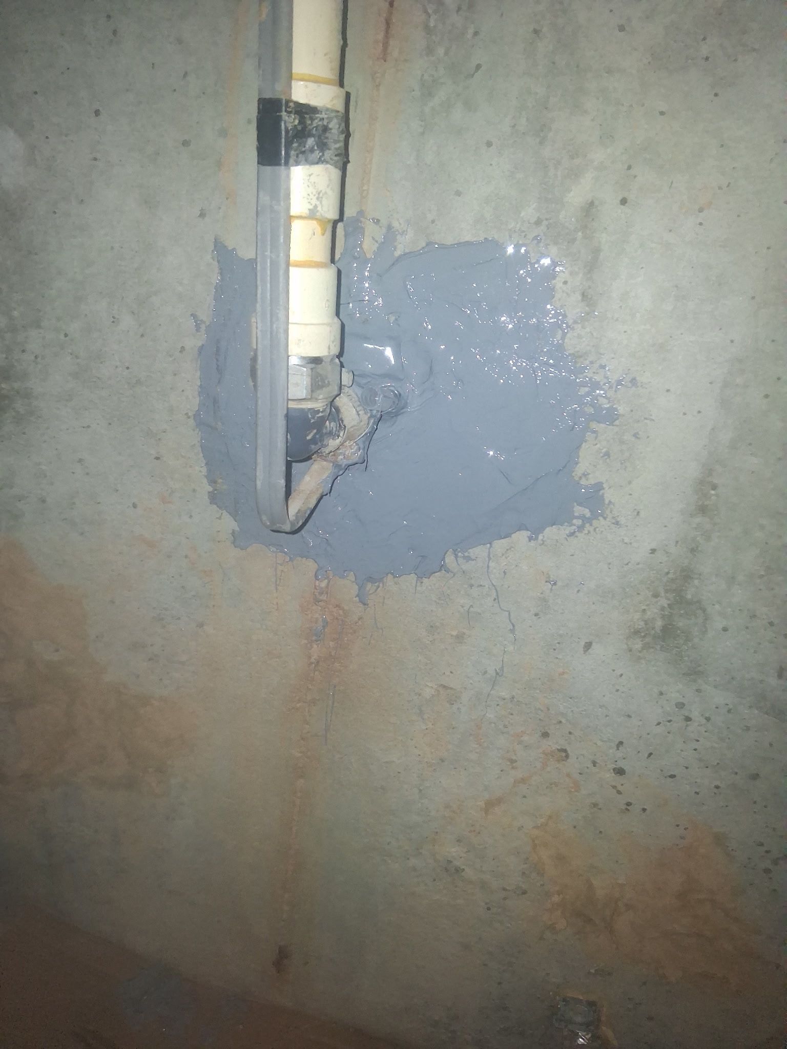 Damaged wall with exposed pipe and patched gray plaster around the hole