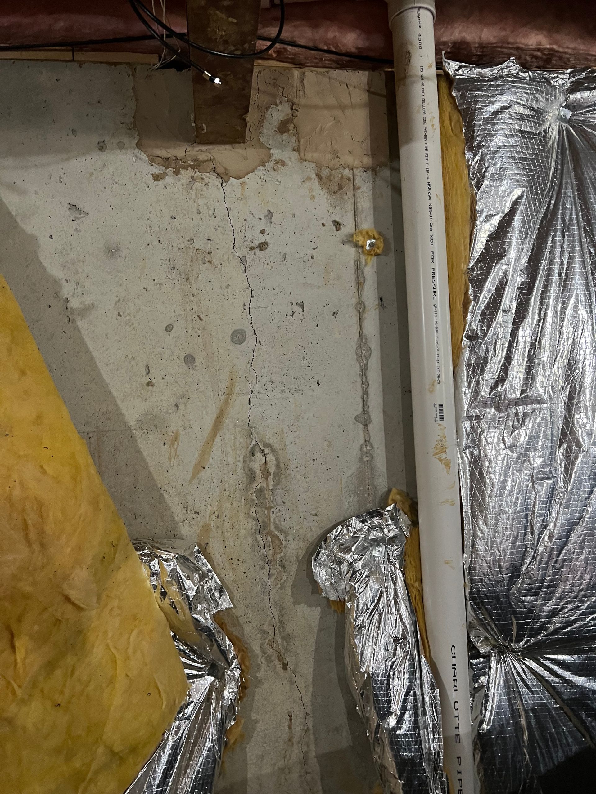 Basement wall with insulated ductwork, foil-covered pipes, and a yellow insulation sheet.