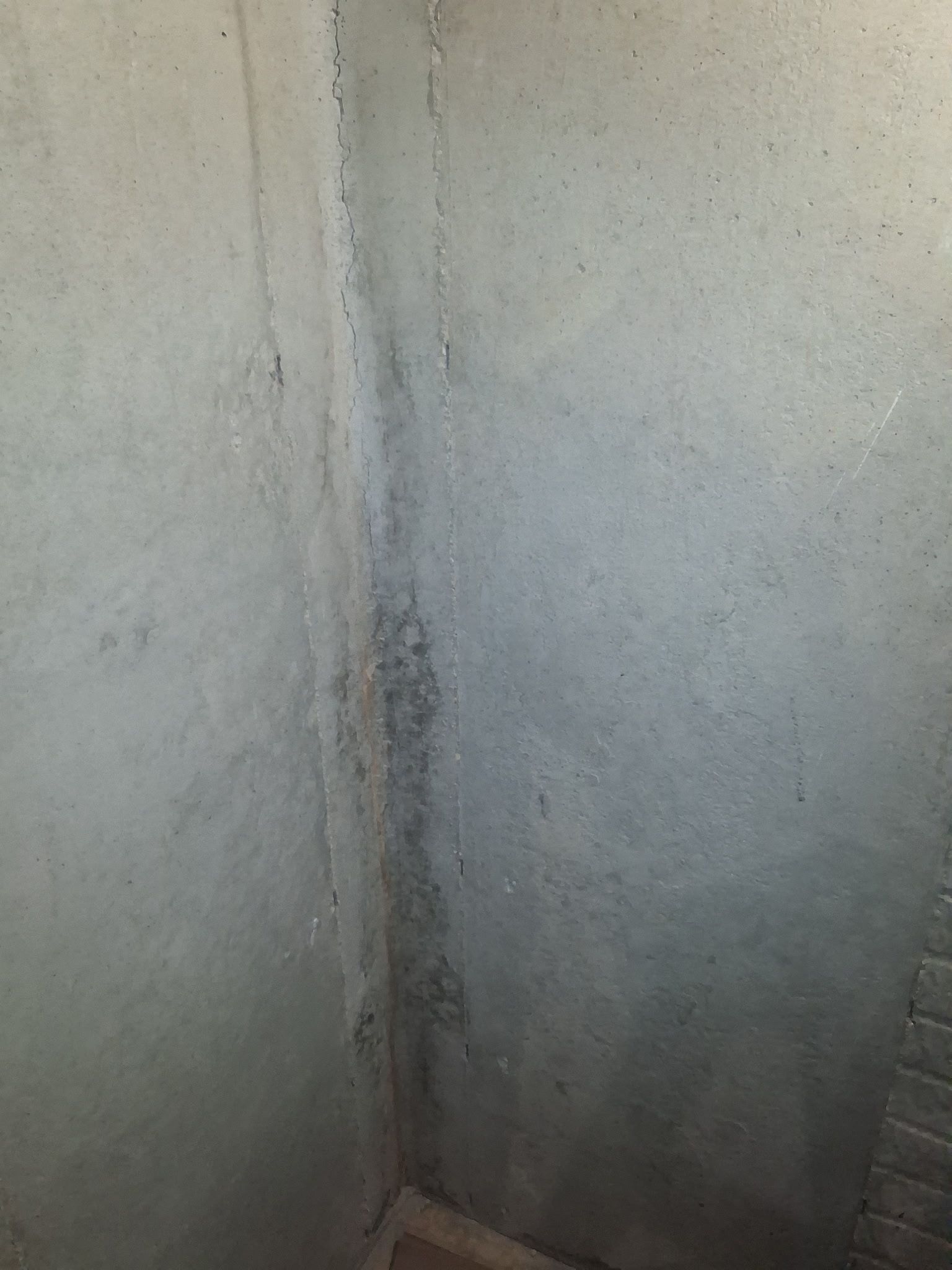 Close-up of a gray concrete wall corner with dark stains and a vertical crack