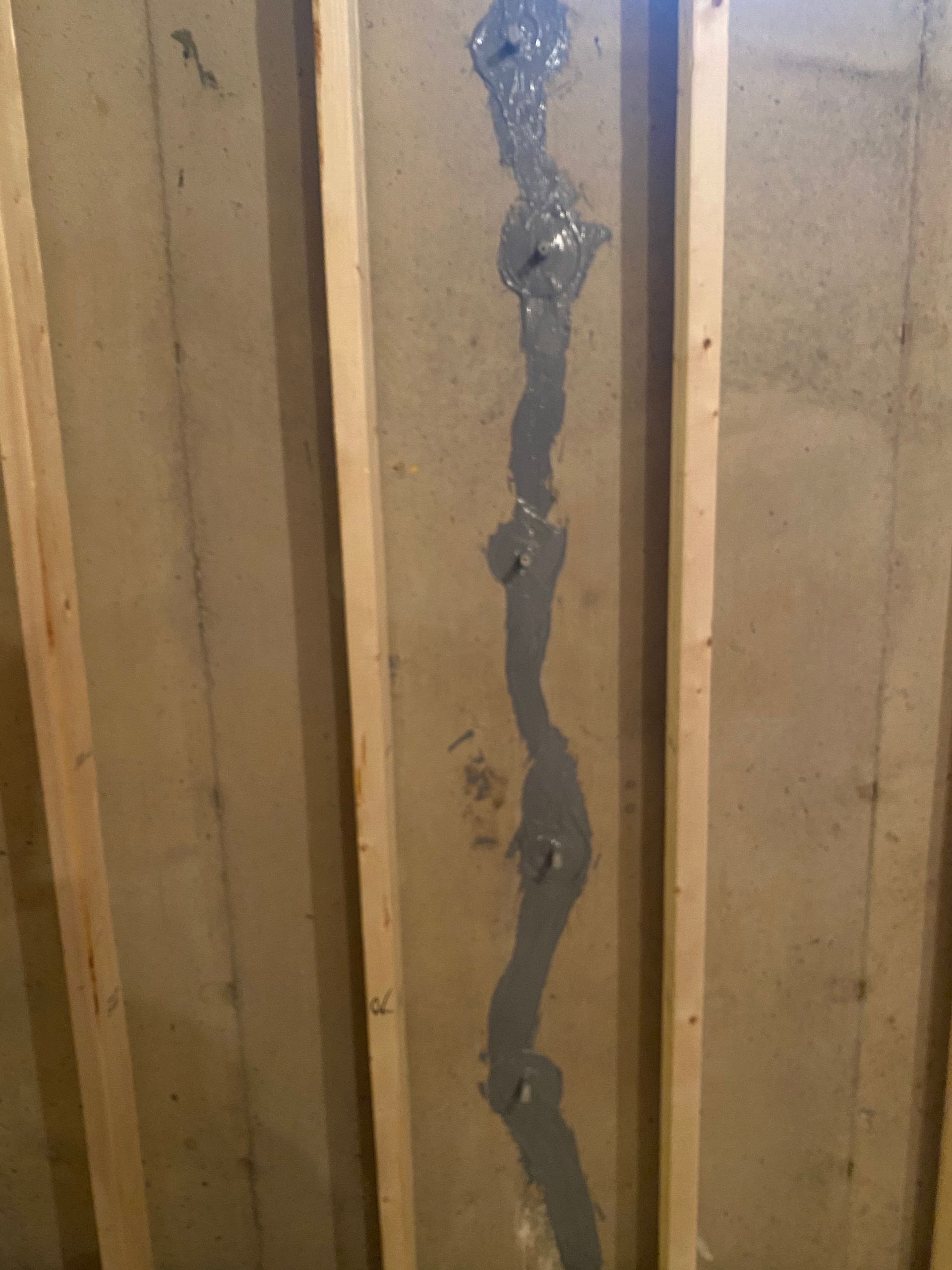 Vertical crack sealed with dark caulk on a beige wooden wall.