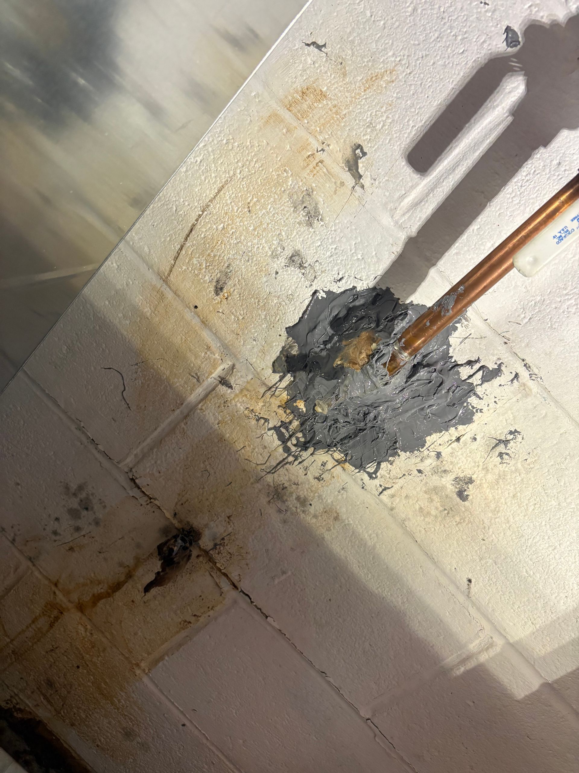 Damaged ceiling with a cracked patch and exposed conduit, lit by sunlight.