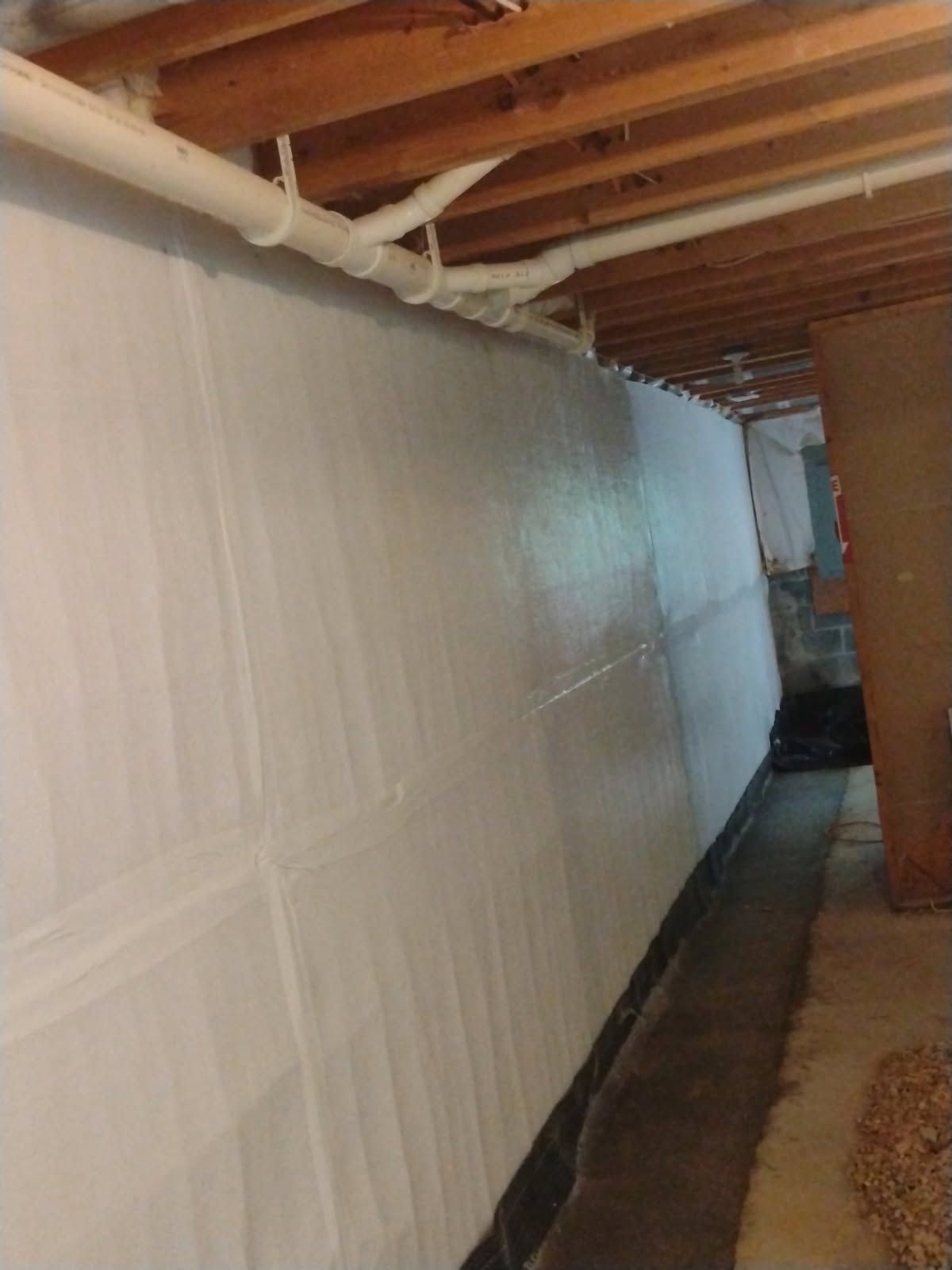 Narrow basement corridor with white plastic sheeting on the left wall and exposed beams overhead