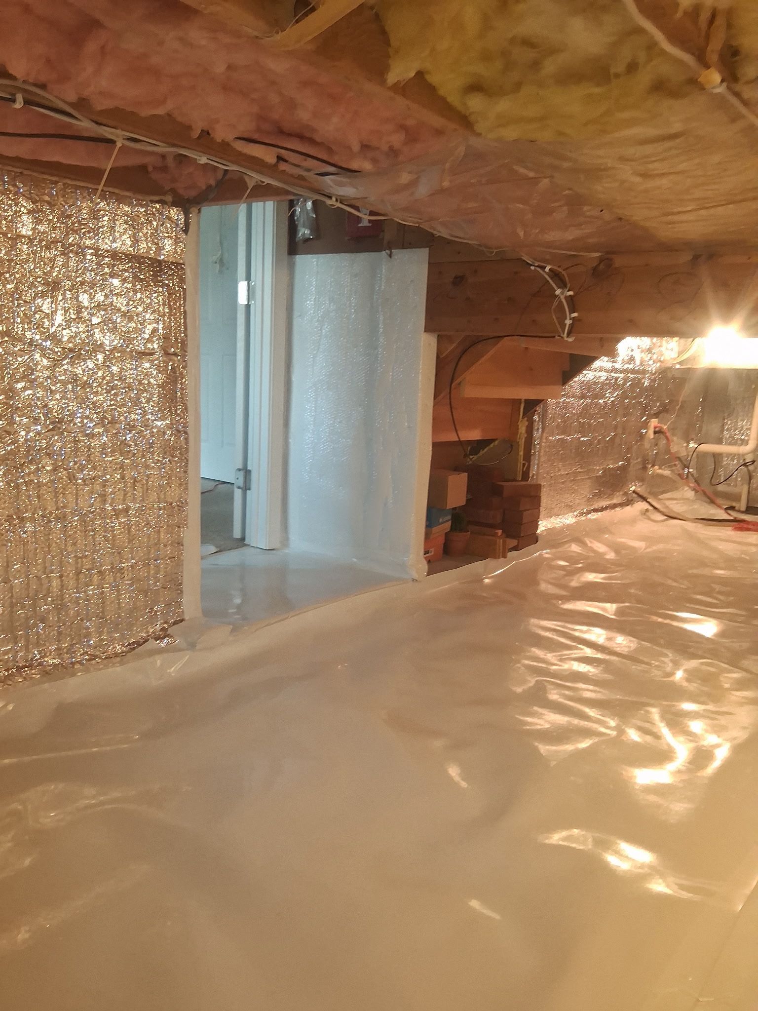 Basement under construction with insulation, exposed beams, and plastic sheeting covering the floor.