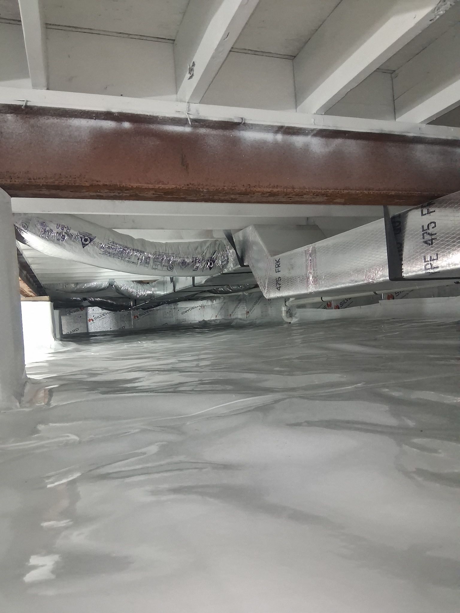 Crawlspace with plastic vapor barrier on the floor and exposed beams, showing low ceiling and ductwork