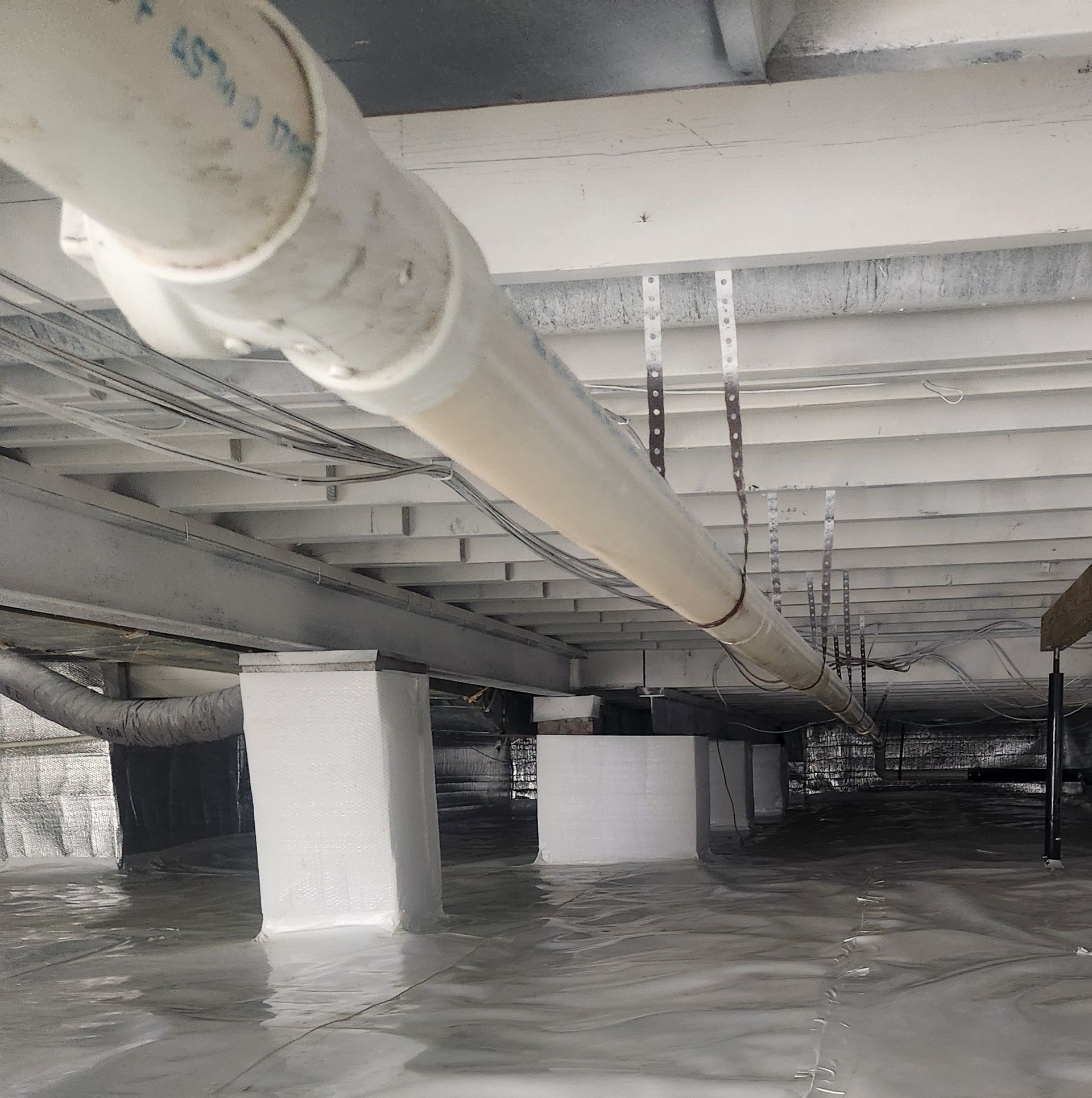 Under a low industrial ceiling, large white pipes run through a flooded basement with standing water.