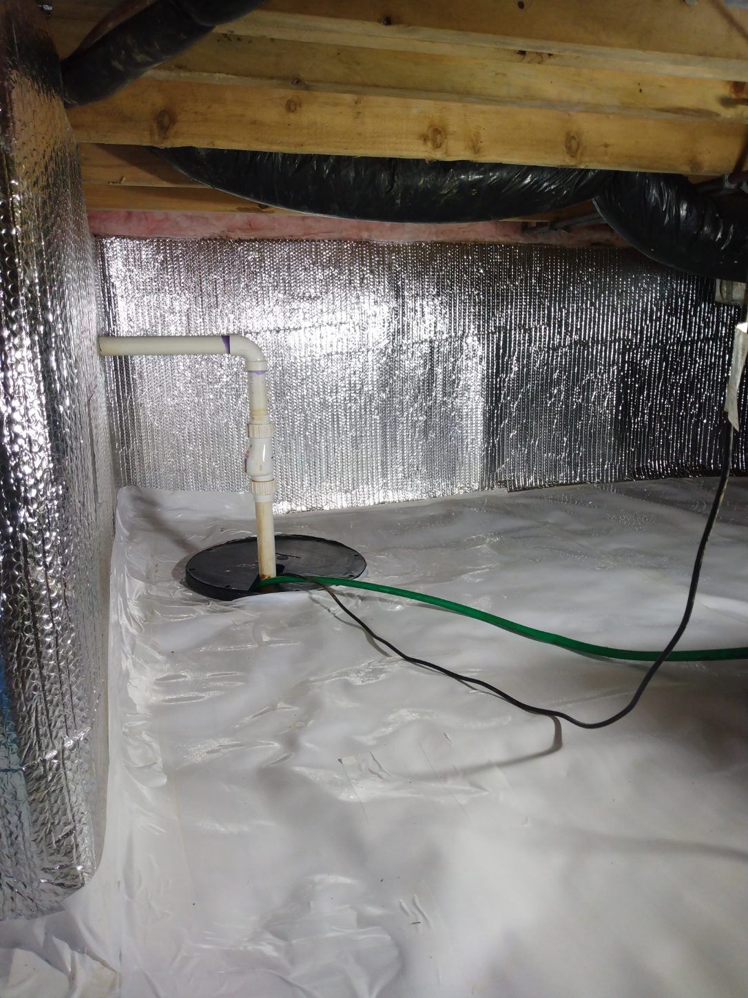 Crawlspace with foil insulation, white floor liner, exposed wooden beams, and a green cable across the floor