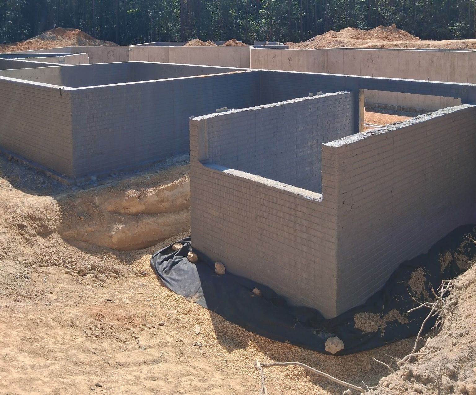 Partially built cinder block structure on a dirt lot, with one small room in the foreground and larger walls behind.