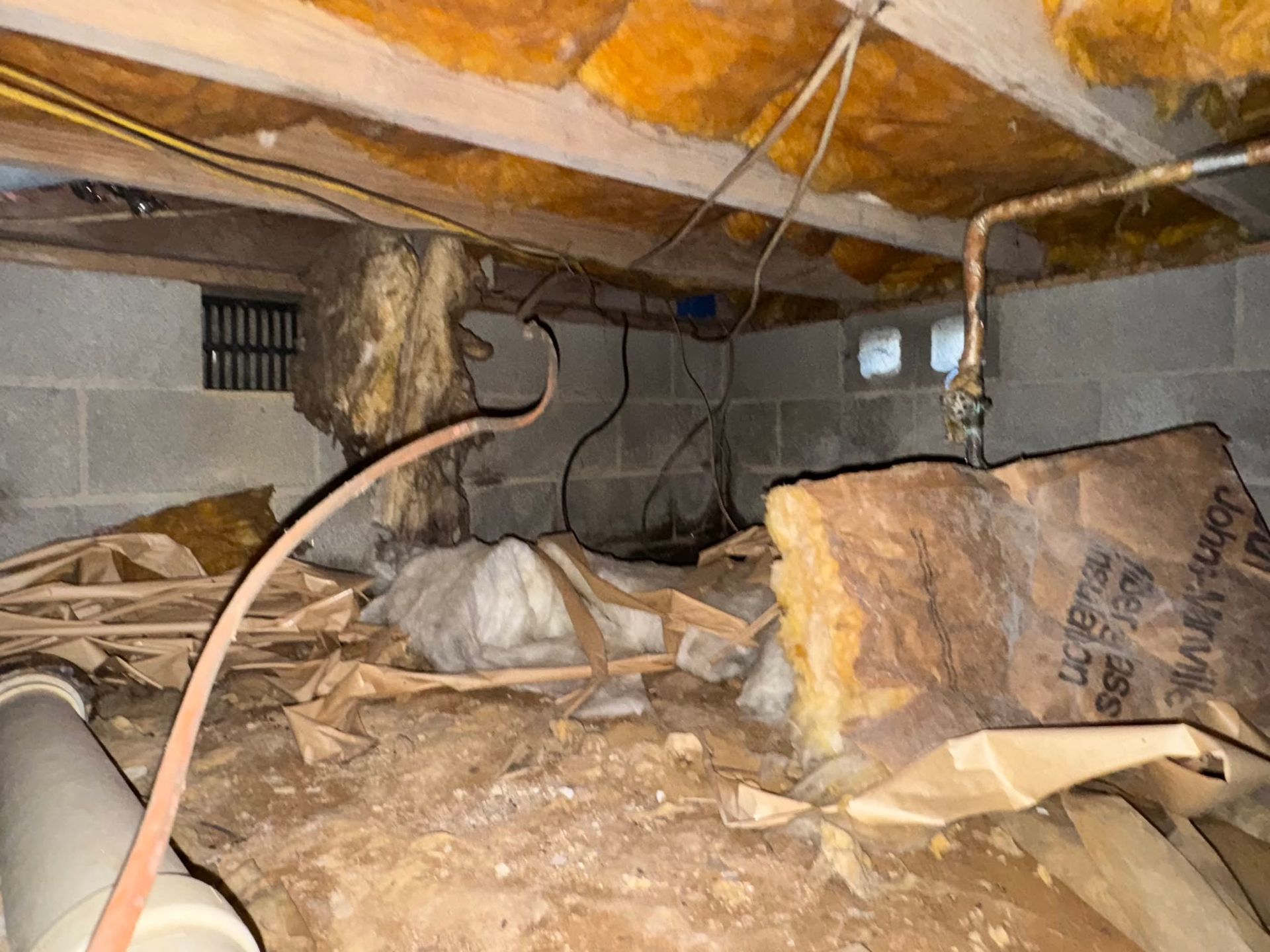 Damaged attic crawlspace with broken insulation, exposed beams, and debris scattered on the floor