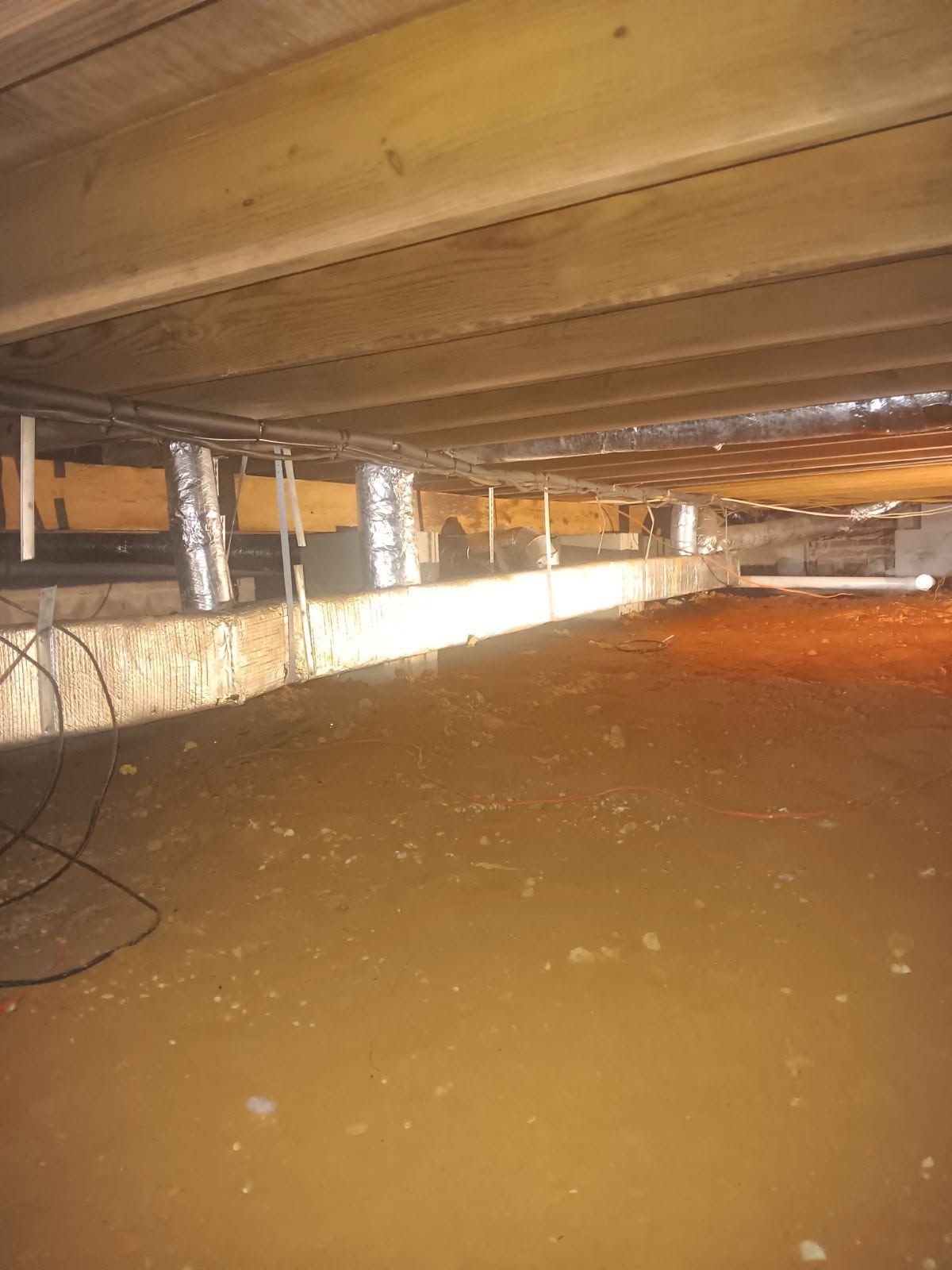 Flooded crawlspace under a wooden floor with support posts and muddy brown water.