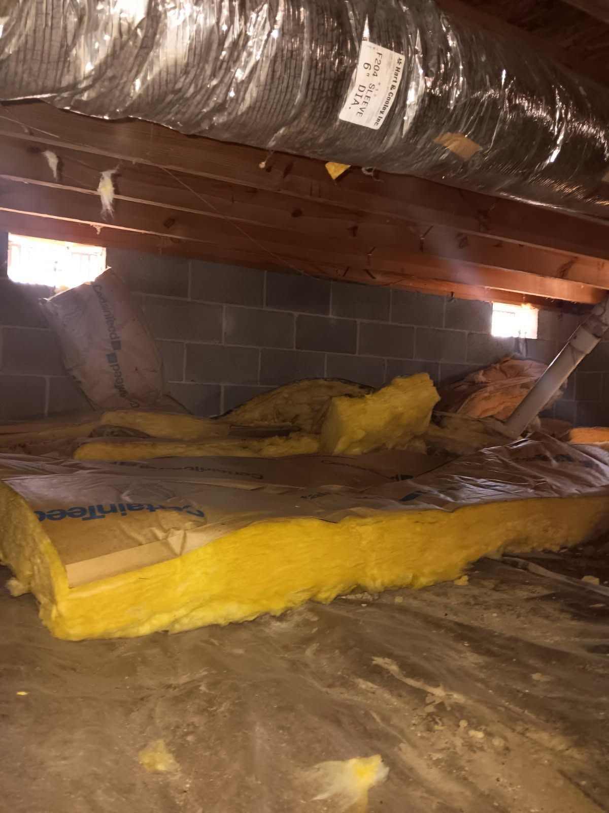 Crawlspace with exposed ductwork, cinderblock wall, and yellow insulation on the floor