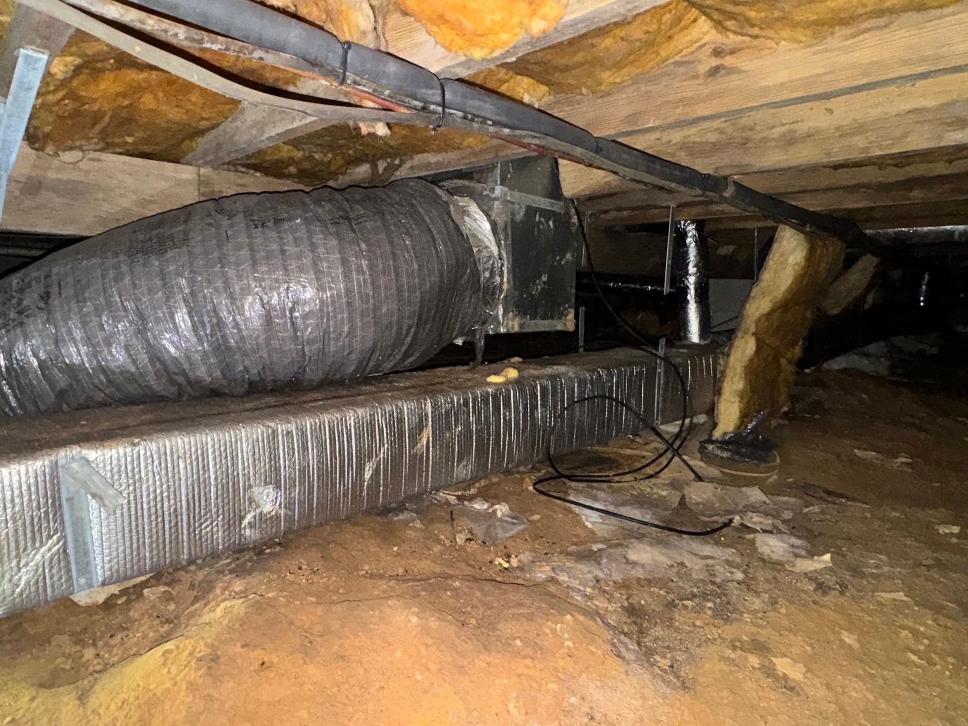 Crawlspace with insulated ductwork, exposed beams, and wiring under a wooden floor