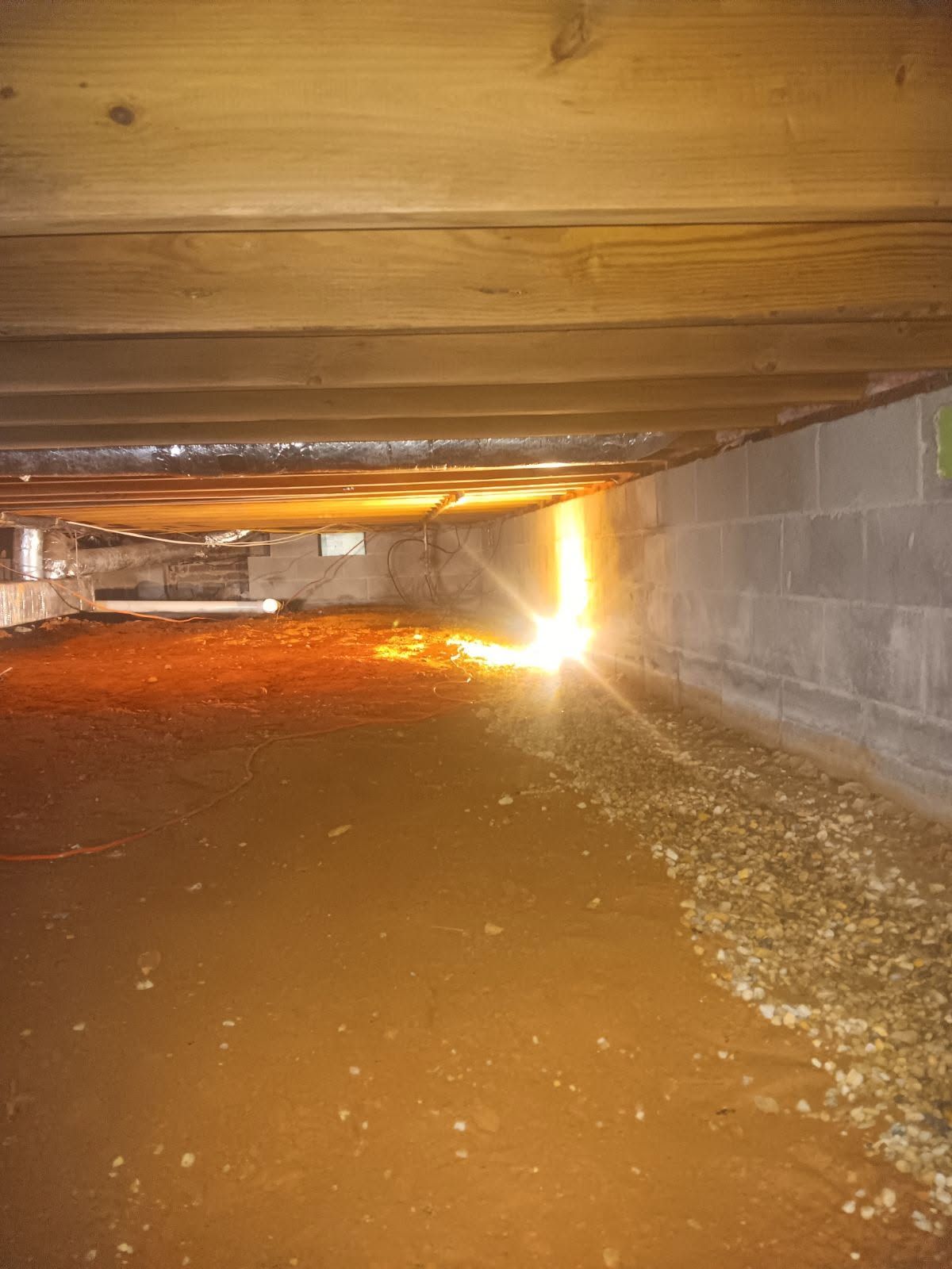Floodwater inside a low crawlspace, with muddy water reflecting light under wooden beams and cinder block walls.
