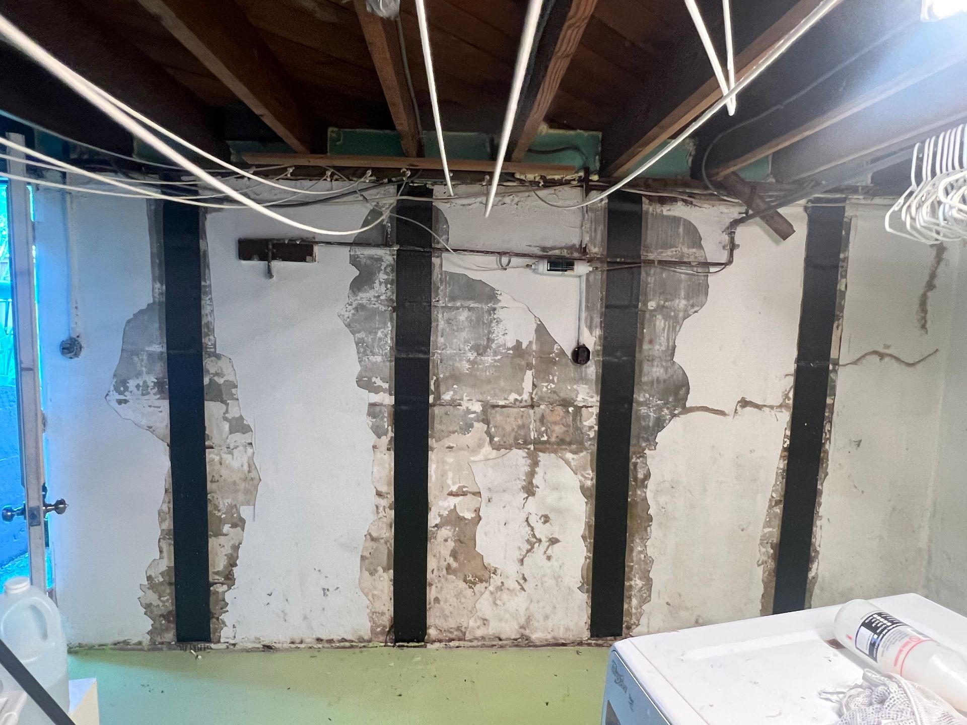 Damaged basement wall with exposed beams, peeling plaster, and construction debris on the floor