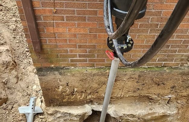 Utility pipes beside a brick wall and a trench dug along the foundation.