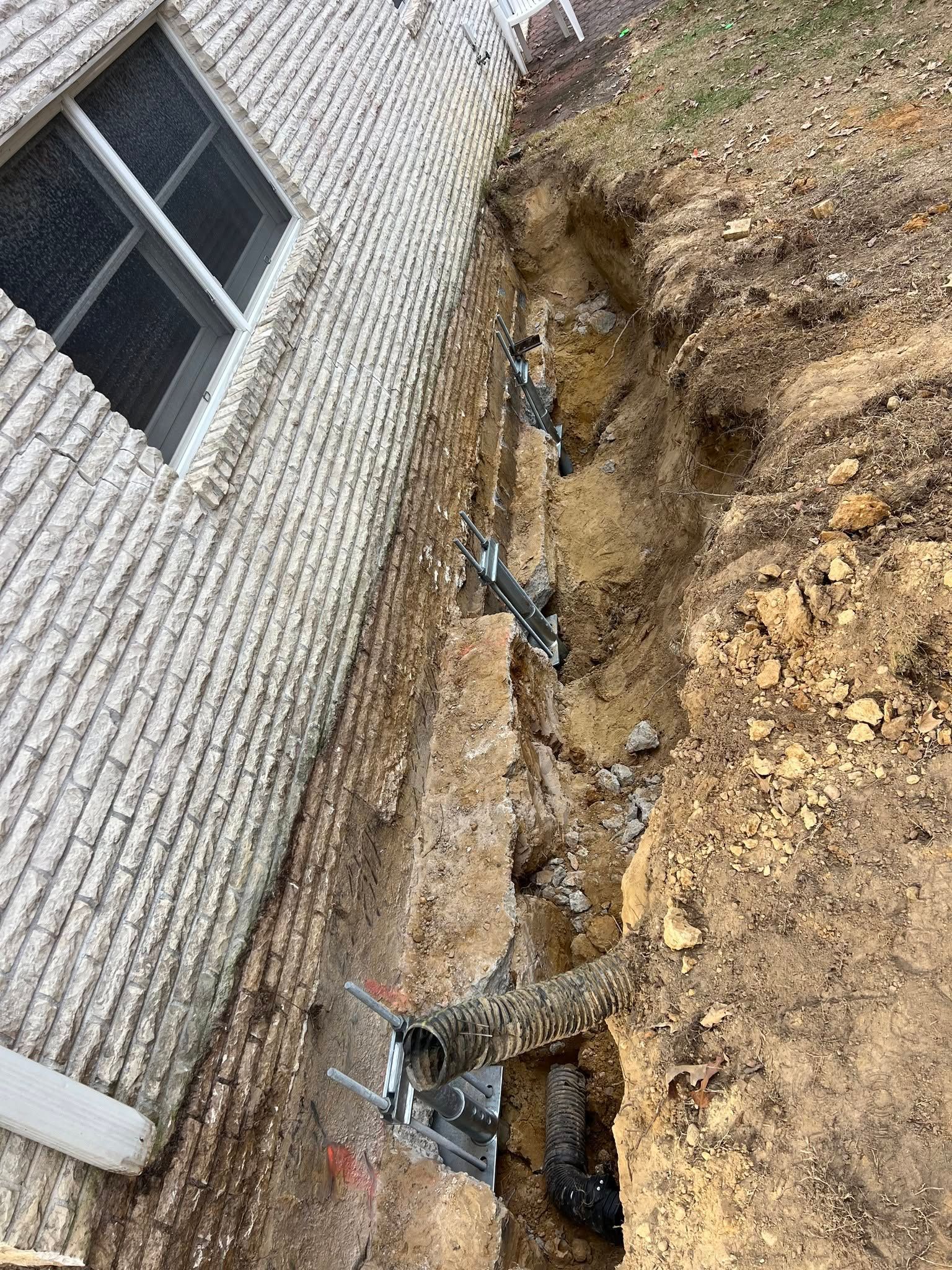 Foundation excavation beside brick house with exposed pipes and dirt trench