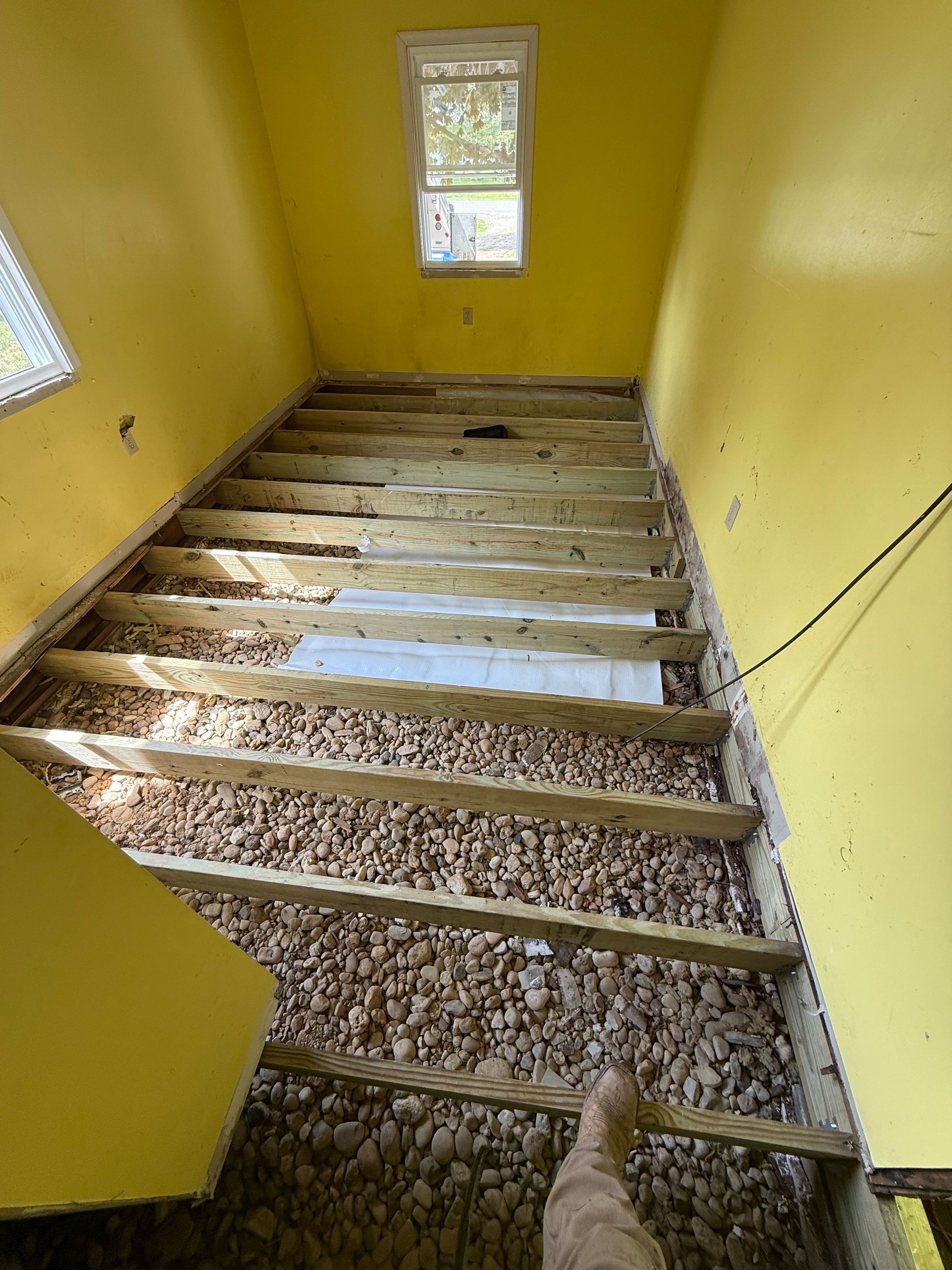 Yellow stairwell with exposed wooden steps and gravel, viewed from the top toward a window below