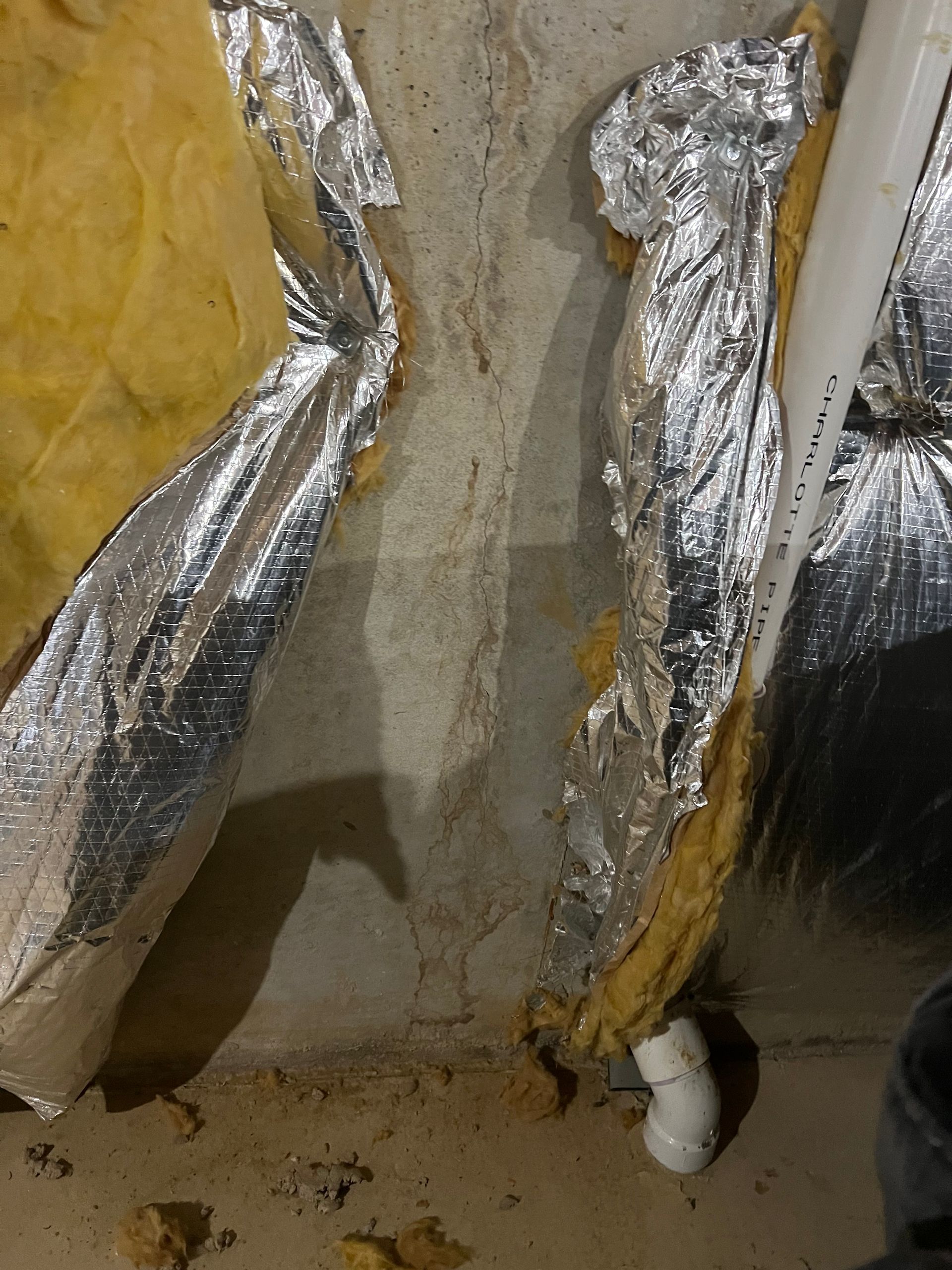 Foil-wrapped insulation around ductwork and a concrete wall in a basement or crawl space.