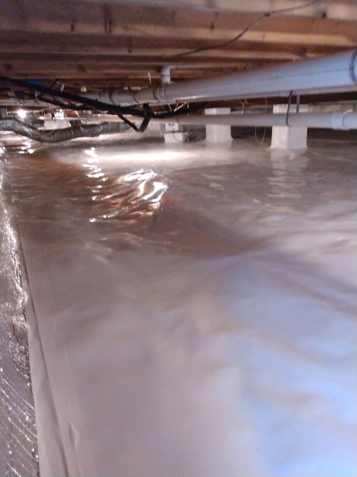 Plastic sheeting in a crawl space beneath floor joists and pipes