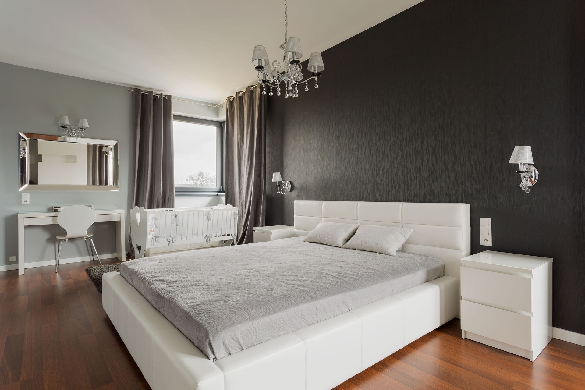 Modern bedroom with white bed, gray bedding, dark gray accent wall, and chandelier.