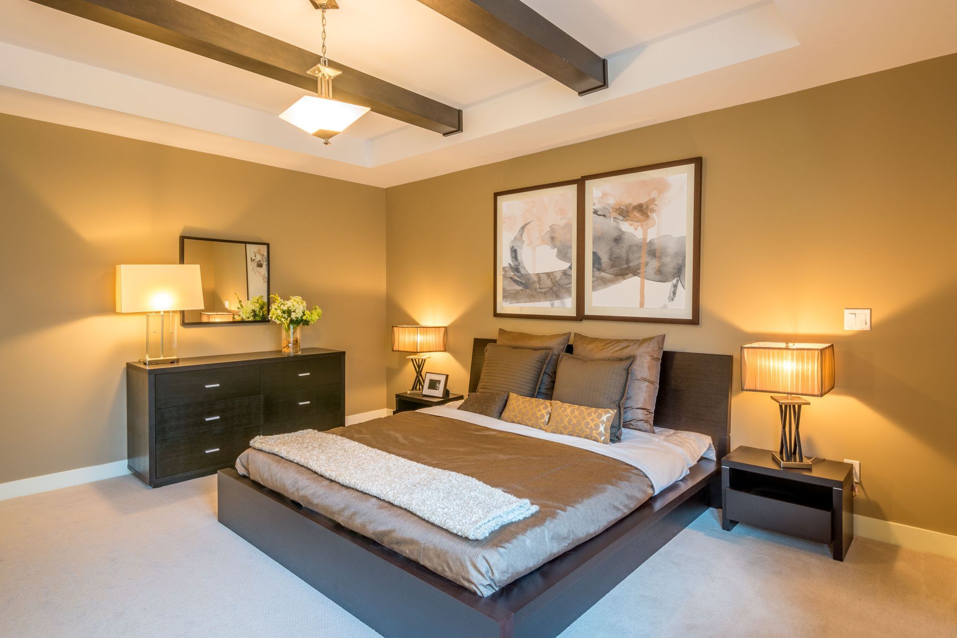 Bedroom with brown and white bedding, a dark dresser, two framed pictures, and warm lighting.