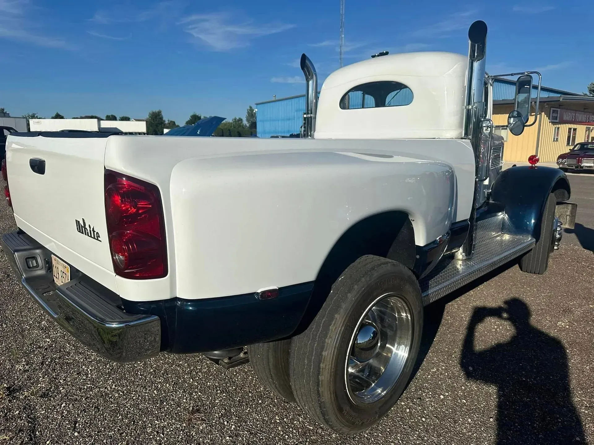 A custom two-tone white and blue pickup truck with dual rear wheels and vertical exhaust stacks parked on gravel.