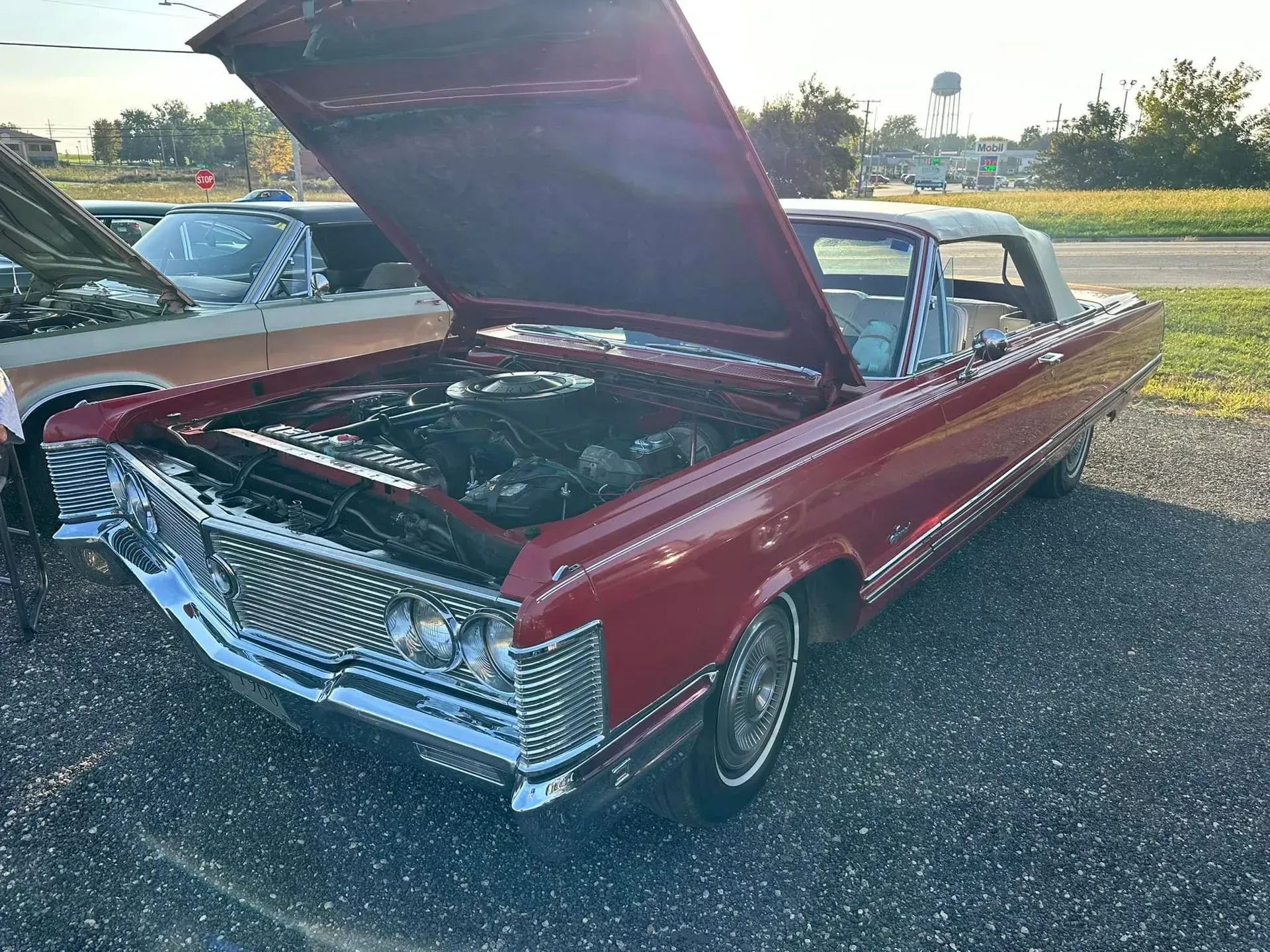 A red classic convertible car with its hood open, parked on a gravel lot during a sunny day.