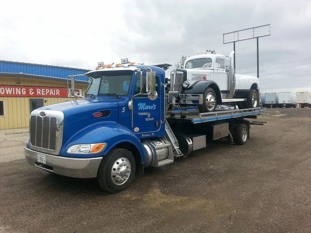 Two blue semi-trucks parked on a gravel lot in front of a building with a red "MARV'S" sign.