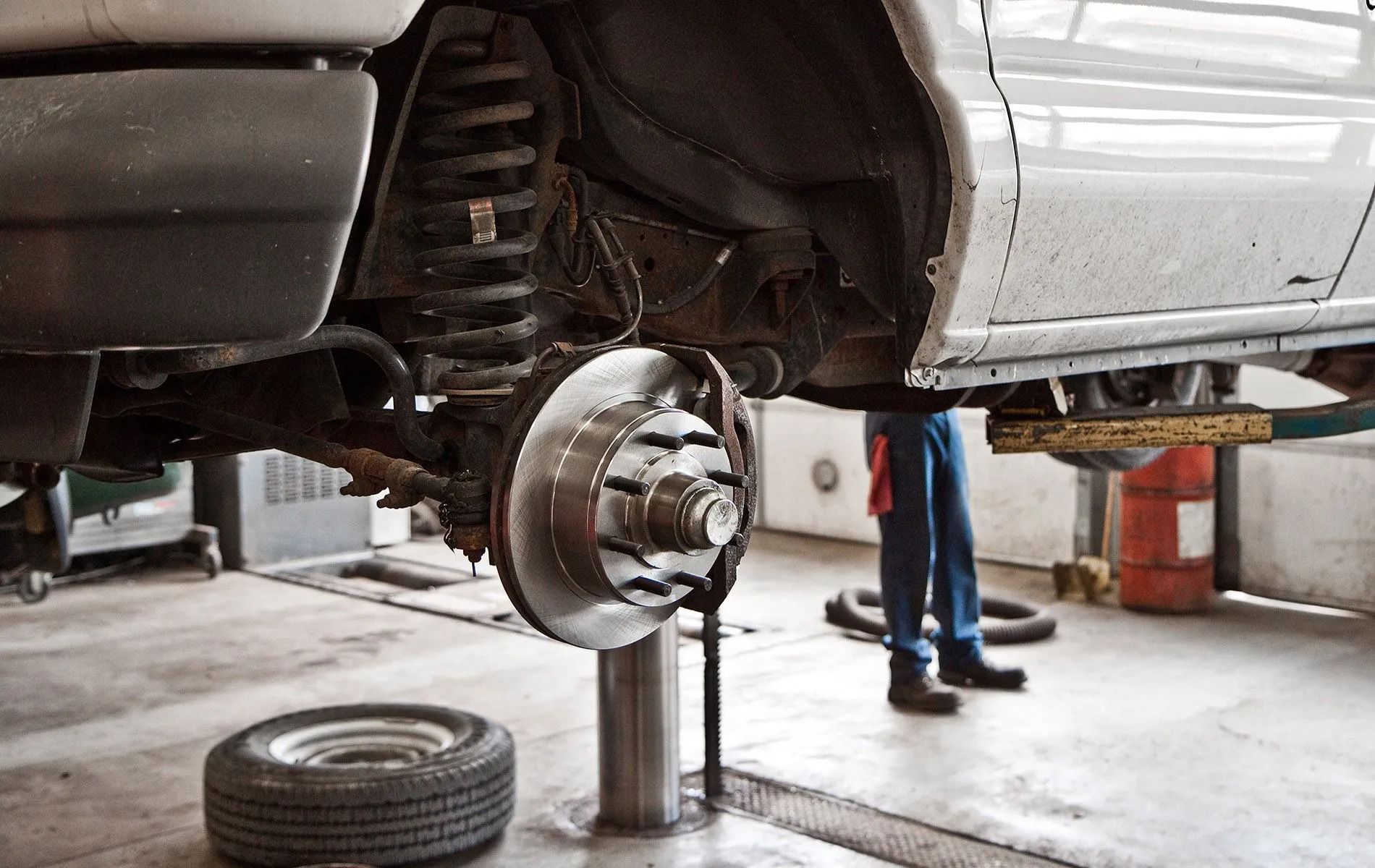 A vehicle raised on a lift in a repair shop with its wheel removed, exposing the brake disc and suspension components.